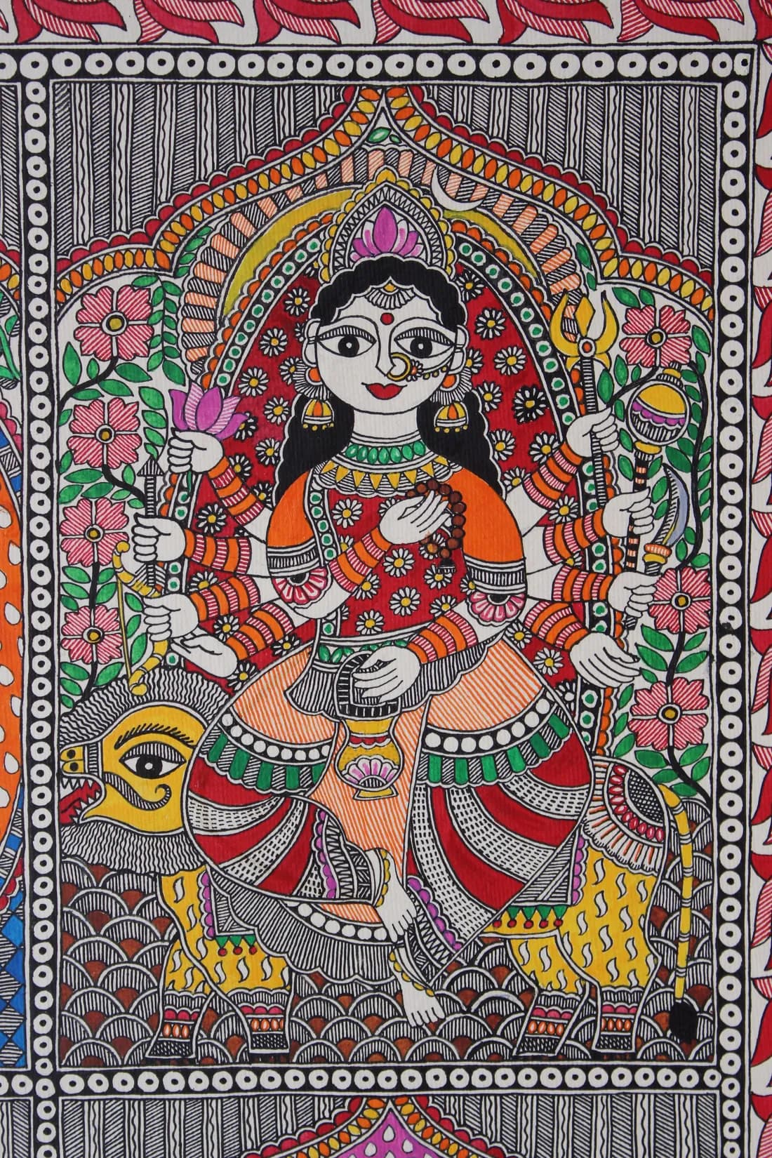 Madhubani painting of a multi-armed goddess holding a lotus, trident and rosary, seated on her lion vahana amid pink floral borders