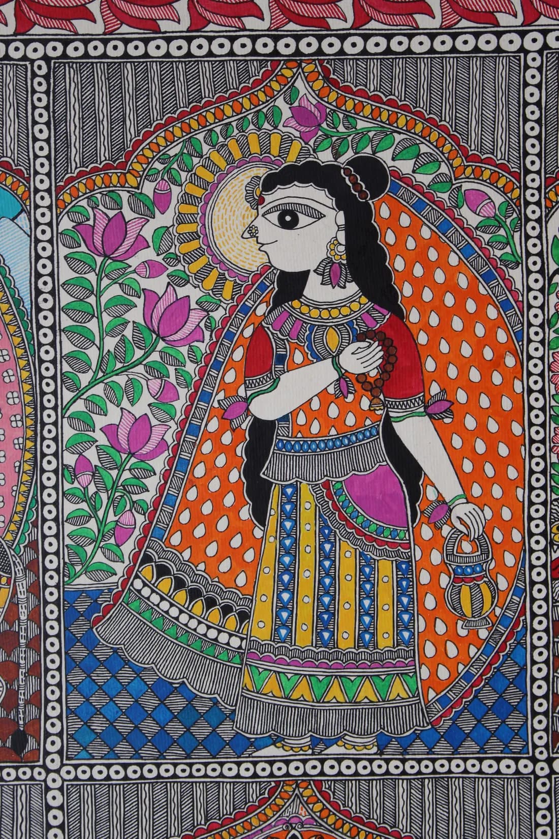 Madhubani painting of a goddess in an orange dotted robe holding a prayer mala and a lamp, framed by a floral arch