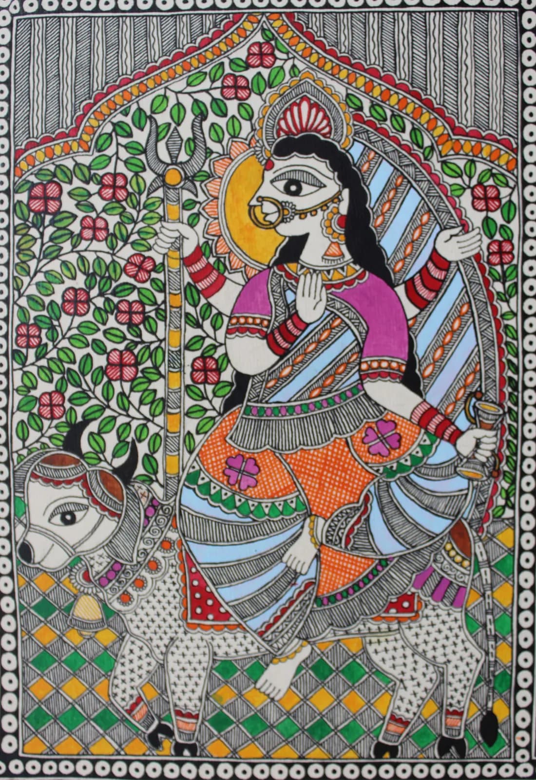 Madhubani painting of a goddess with folded hands holding a trident, seated beside her cow vahana beneath a flowering vine border
