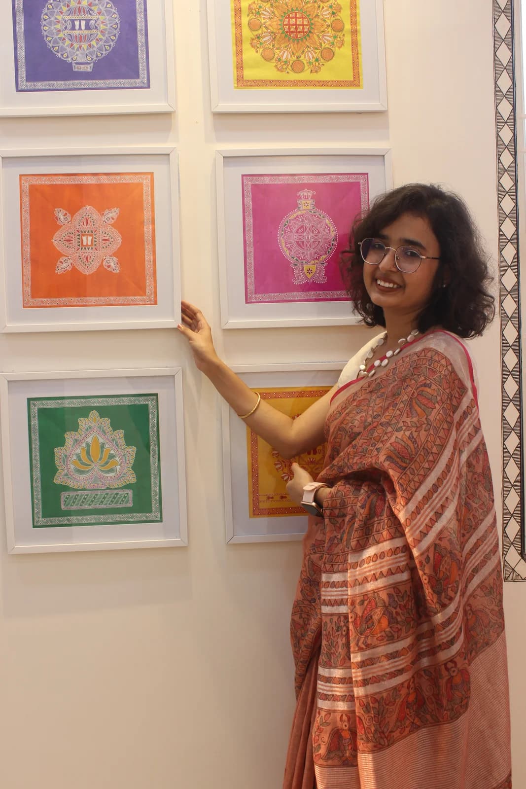 Urwashi Nirala pointing to a row of small, brightly coloured Madhubani motif paintings displayed on her studio wall
